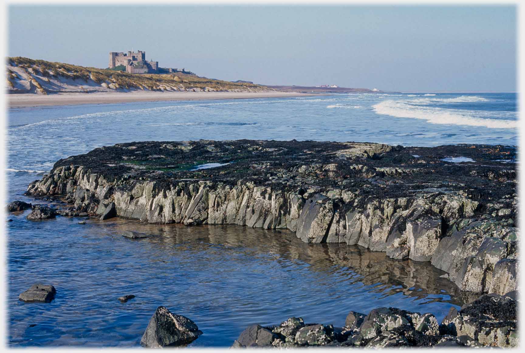 Rocks projecting into the sea with castle beyond.