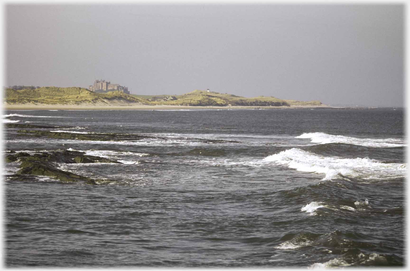 Sea with castle above dunes.