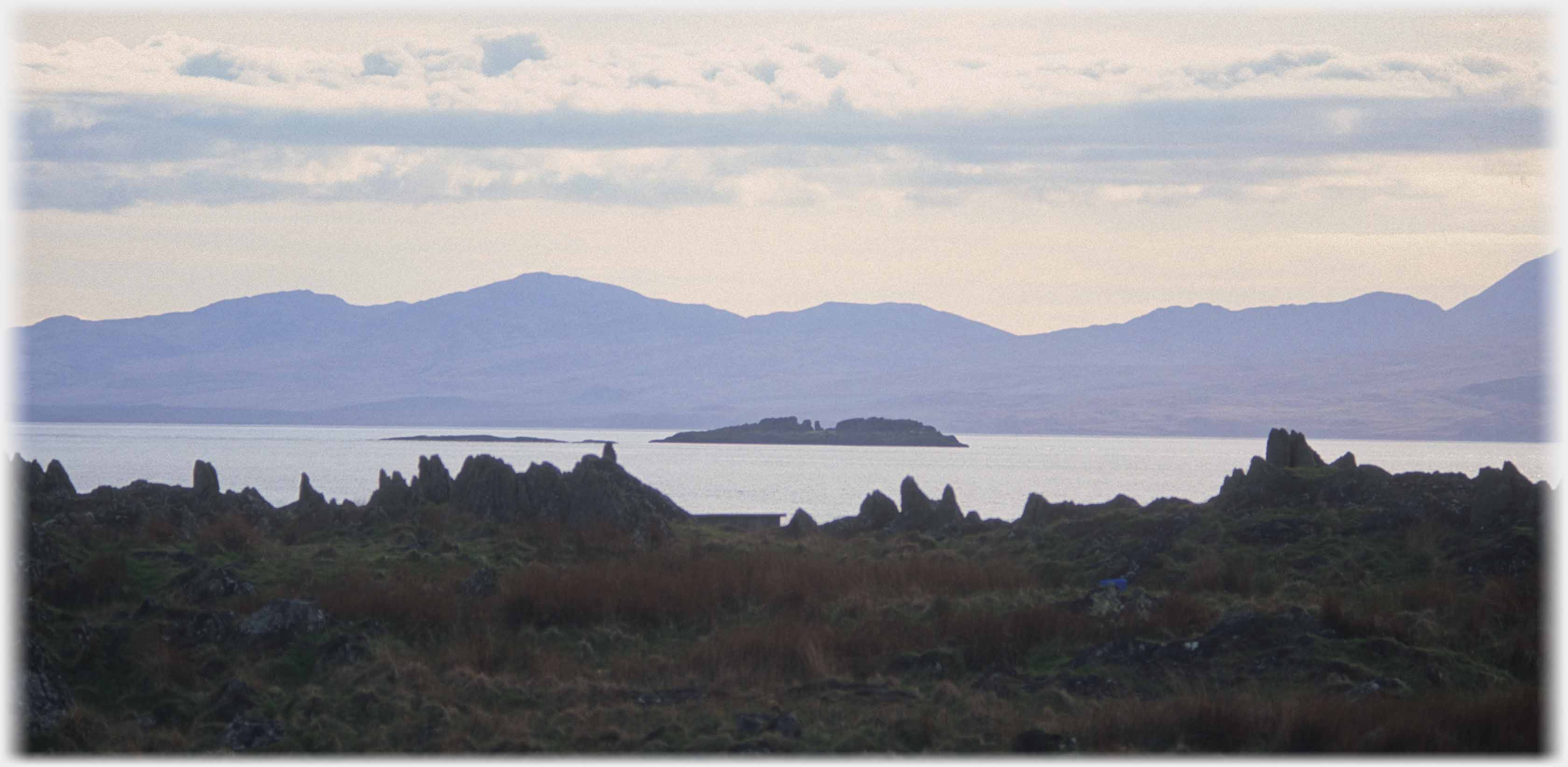 Jagged like of rocks with sea and hills beyond.