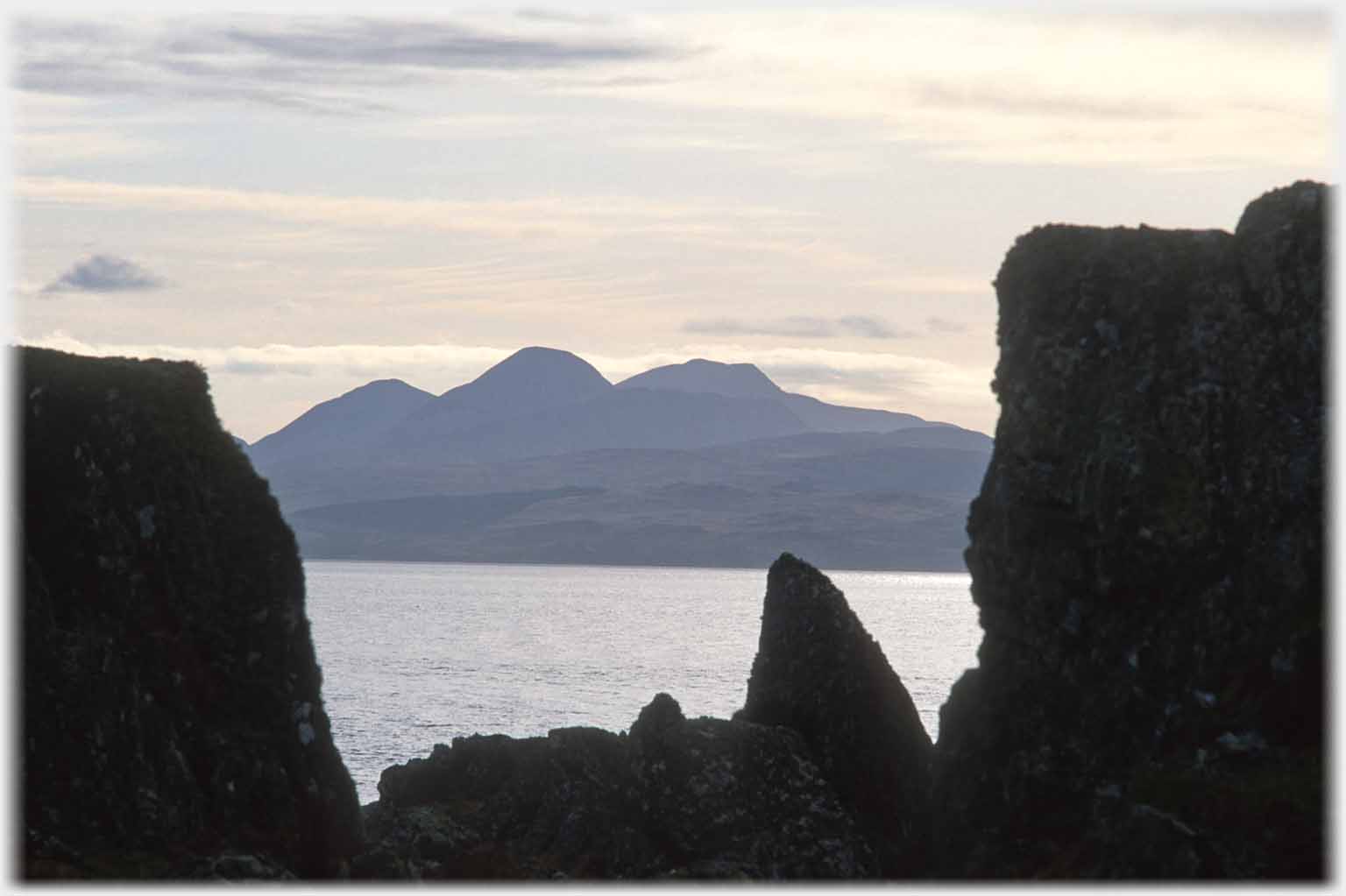 Two big rocks framing view of Jura hills across sea.