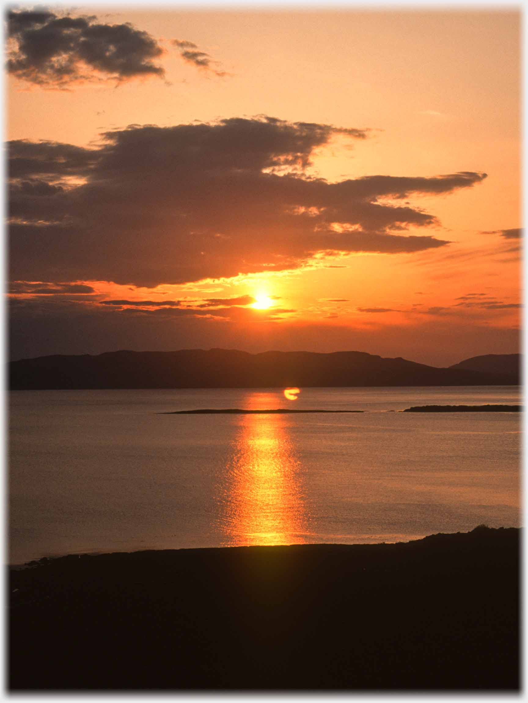 Setting sun above hills across water.