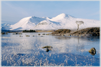 Snow covered hills beyond frozen loch.