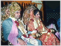 Couple on golden throans adorned with flowers and banknotes.