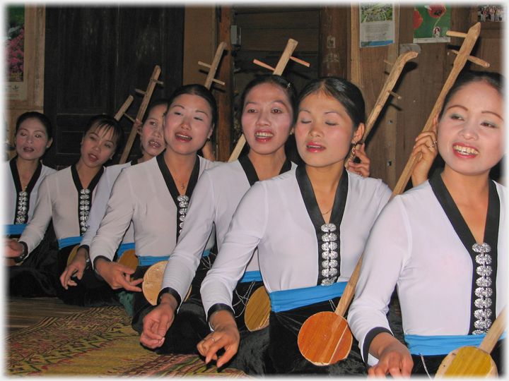 Seven women sitting on the ground with mock instraments.