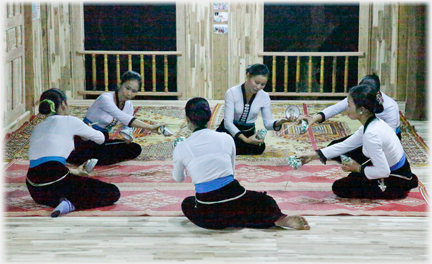 Six women on the ground swaying, holding bowls.
