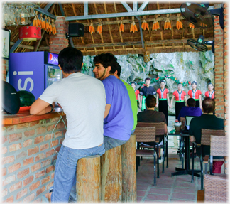 Men at bar on stools, dancers byond.