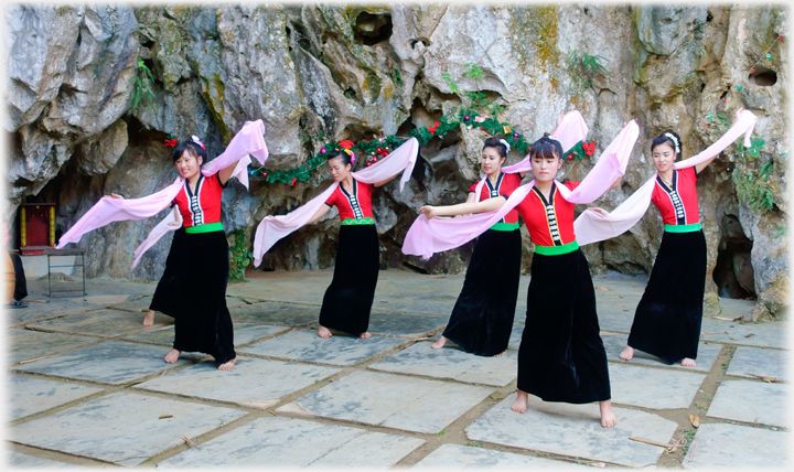 Six women in bare feet dancing with pink scarves on stone floor.