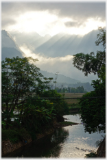 Light shafts between hills and clouds with river in foreground.