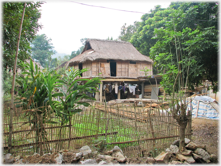 Thai house with wicket fenced vegetables and piled chattels.