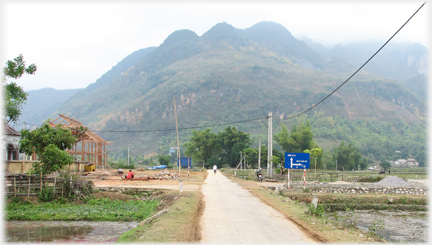 Road pointing at hills with building frame to left.