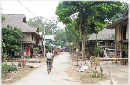 Narrow paved road running between houses with a cyclist .