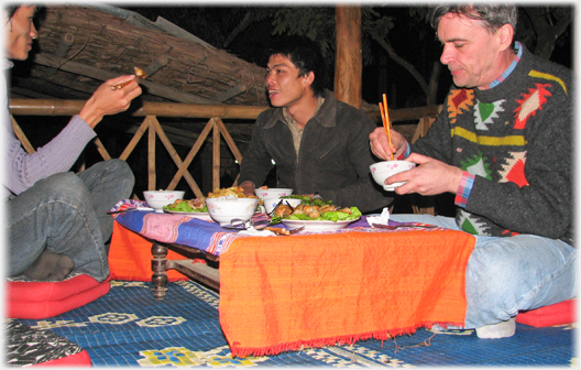 Westerner aand two Vietnamese sitting on the floor and eating at a low table.