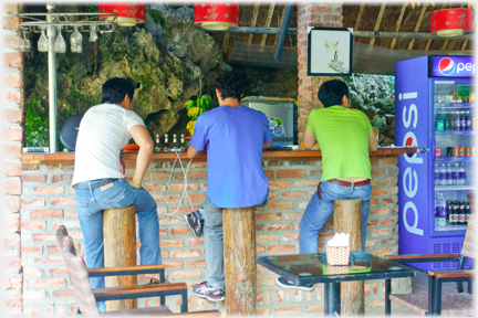 Three men sitting on near metre high tree trunks at a bar.