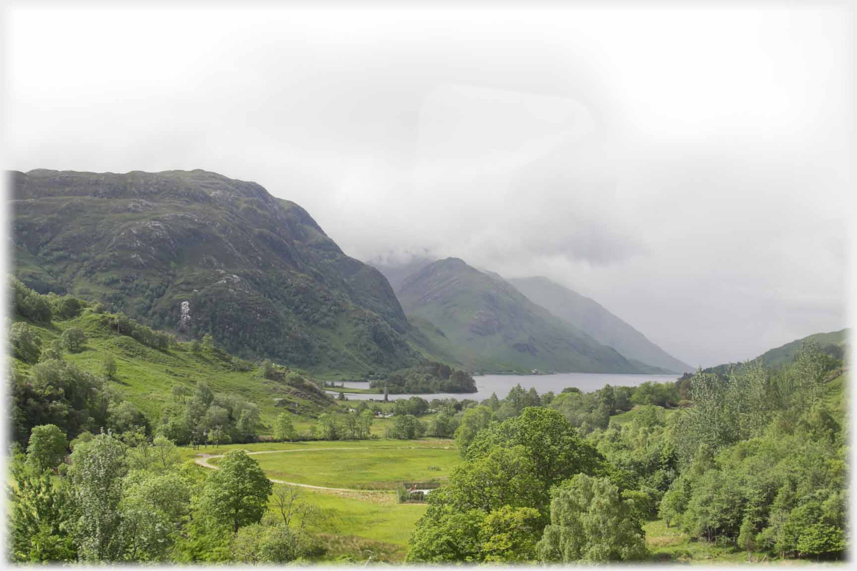 Treed valley, distant water under hills.