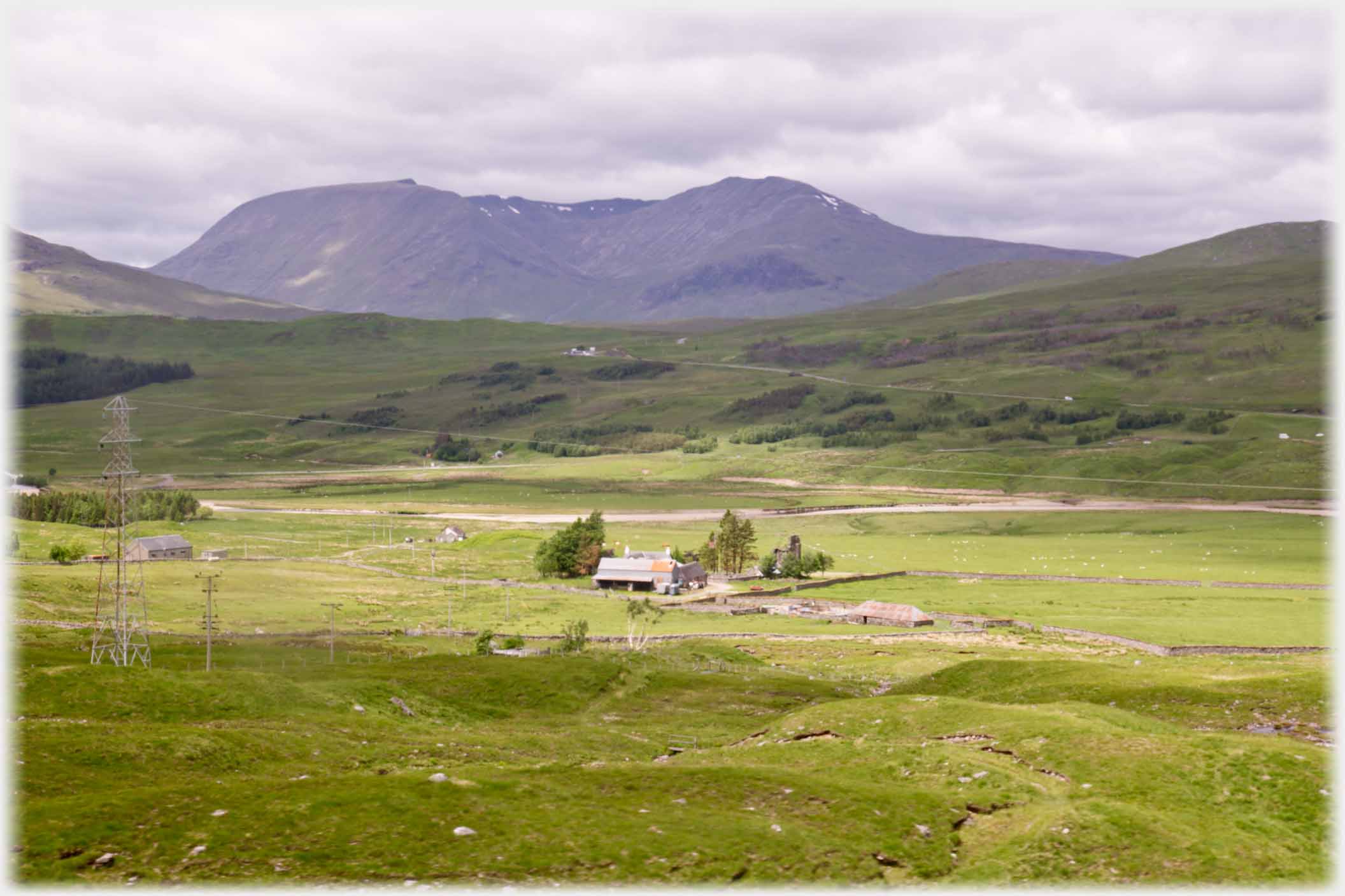 Farm in green landscape with mountains beyond.