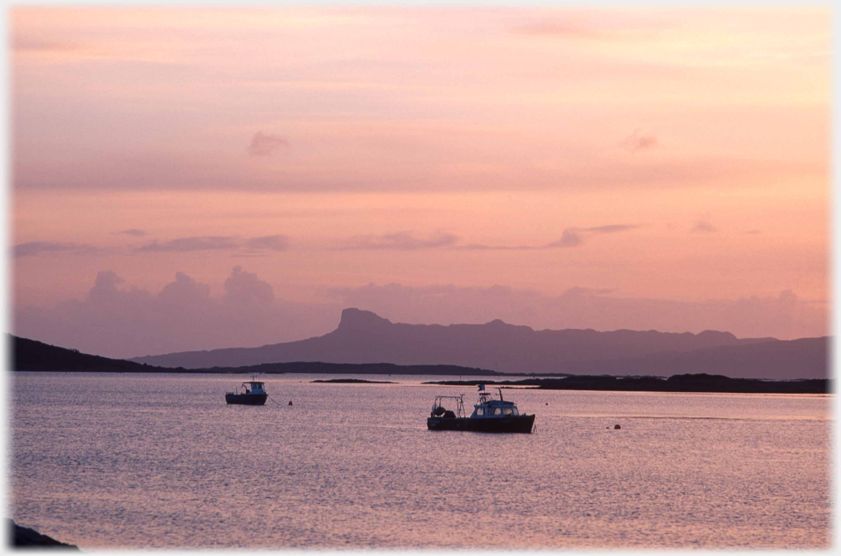 Fishing boat on pink sea with the unique profile of Eigg beyond.