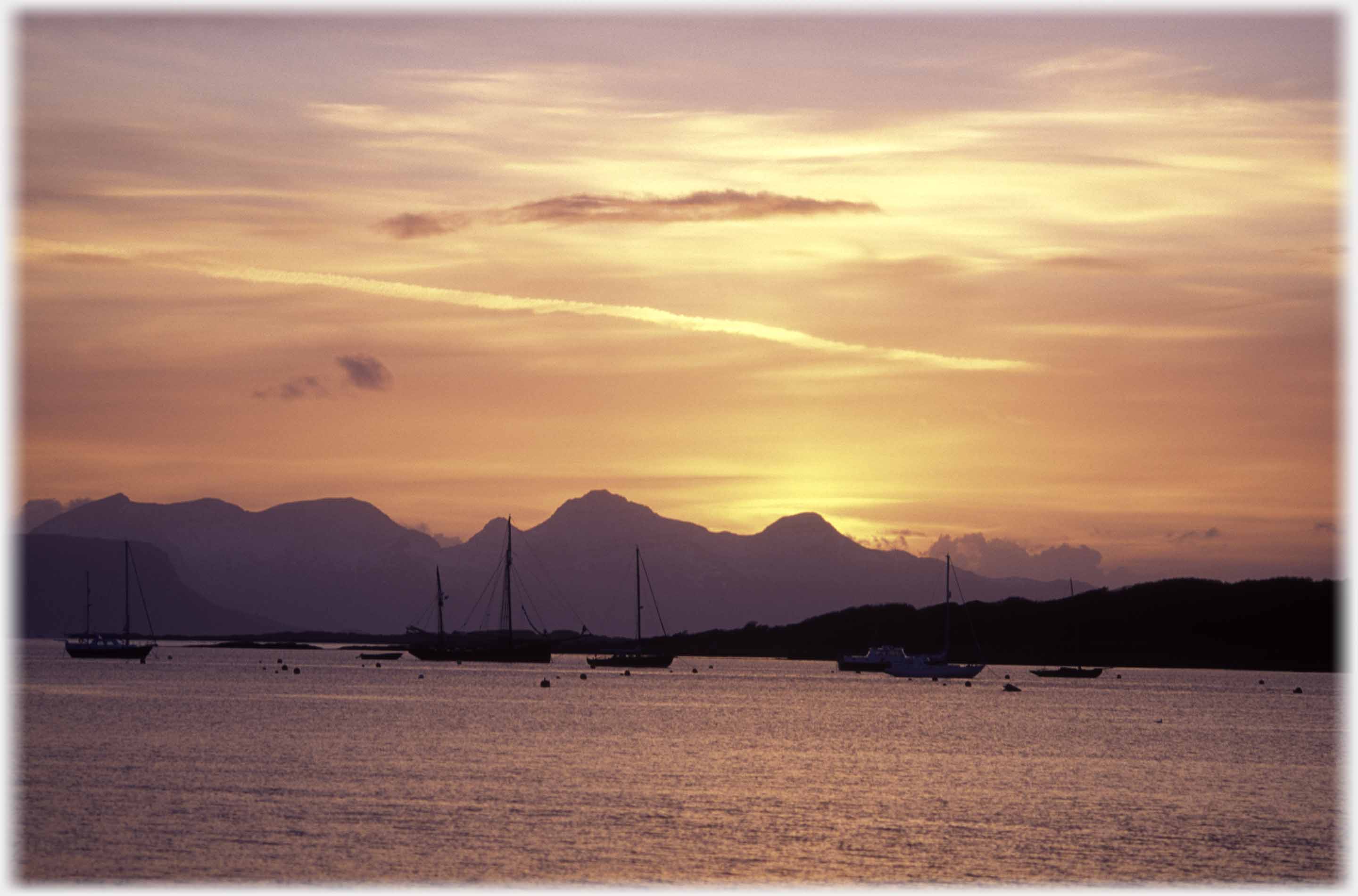 Sun behind hills, a number of moured yachts.