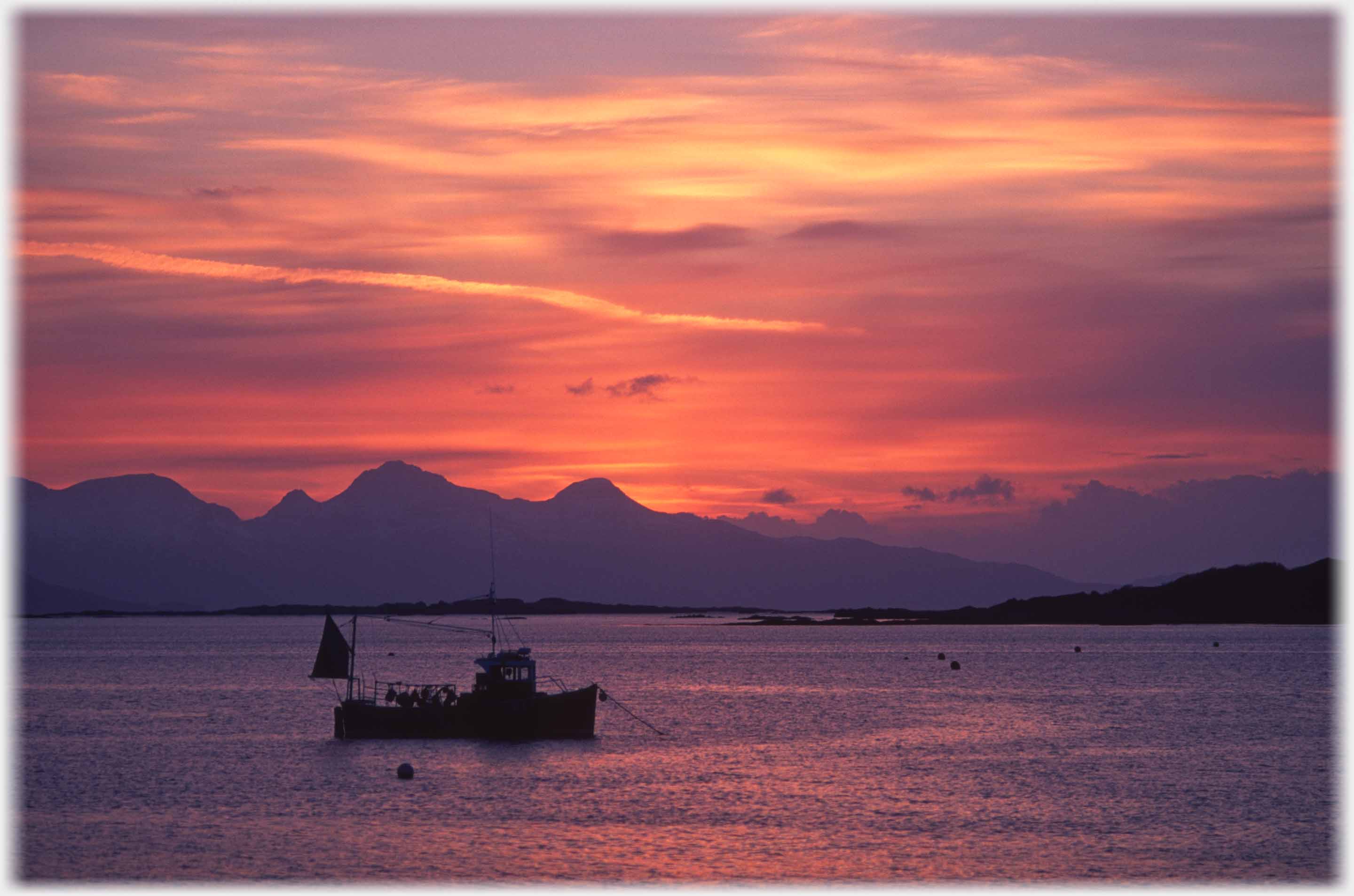 Fishing boat dark with end of red sunset in sky.