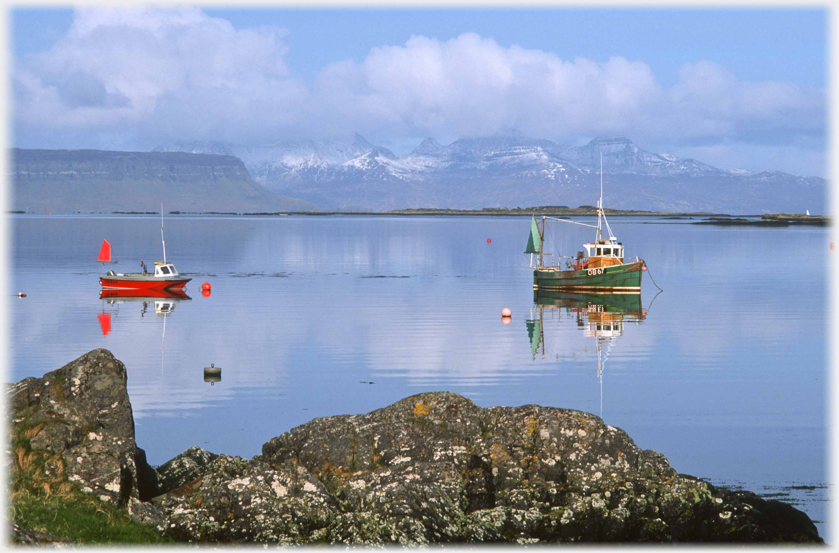 Red and green boats and their reflections on still blue sea.