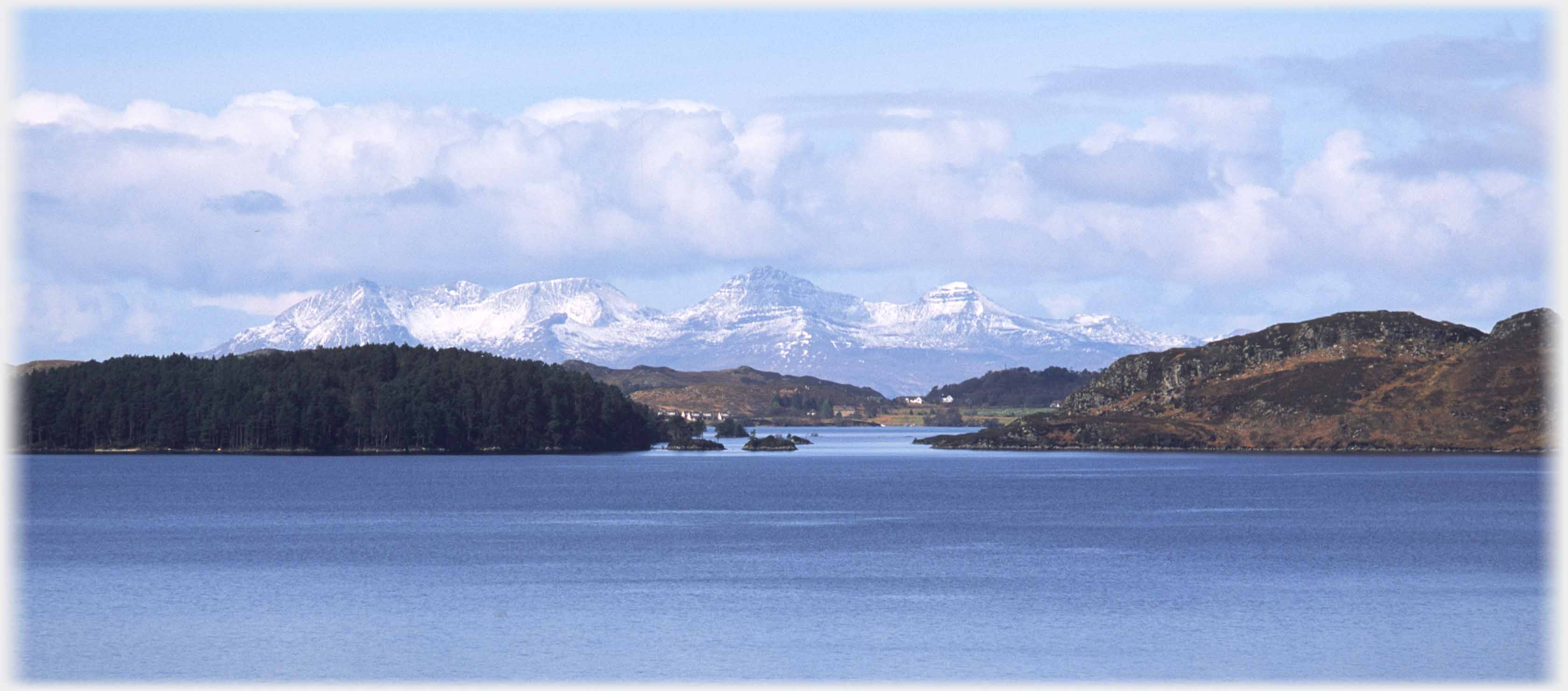 Snow covered hills behind lower nearer hills at head of loch.