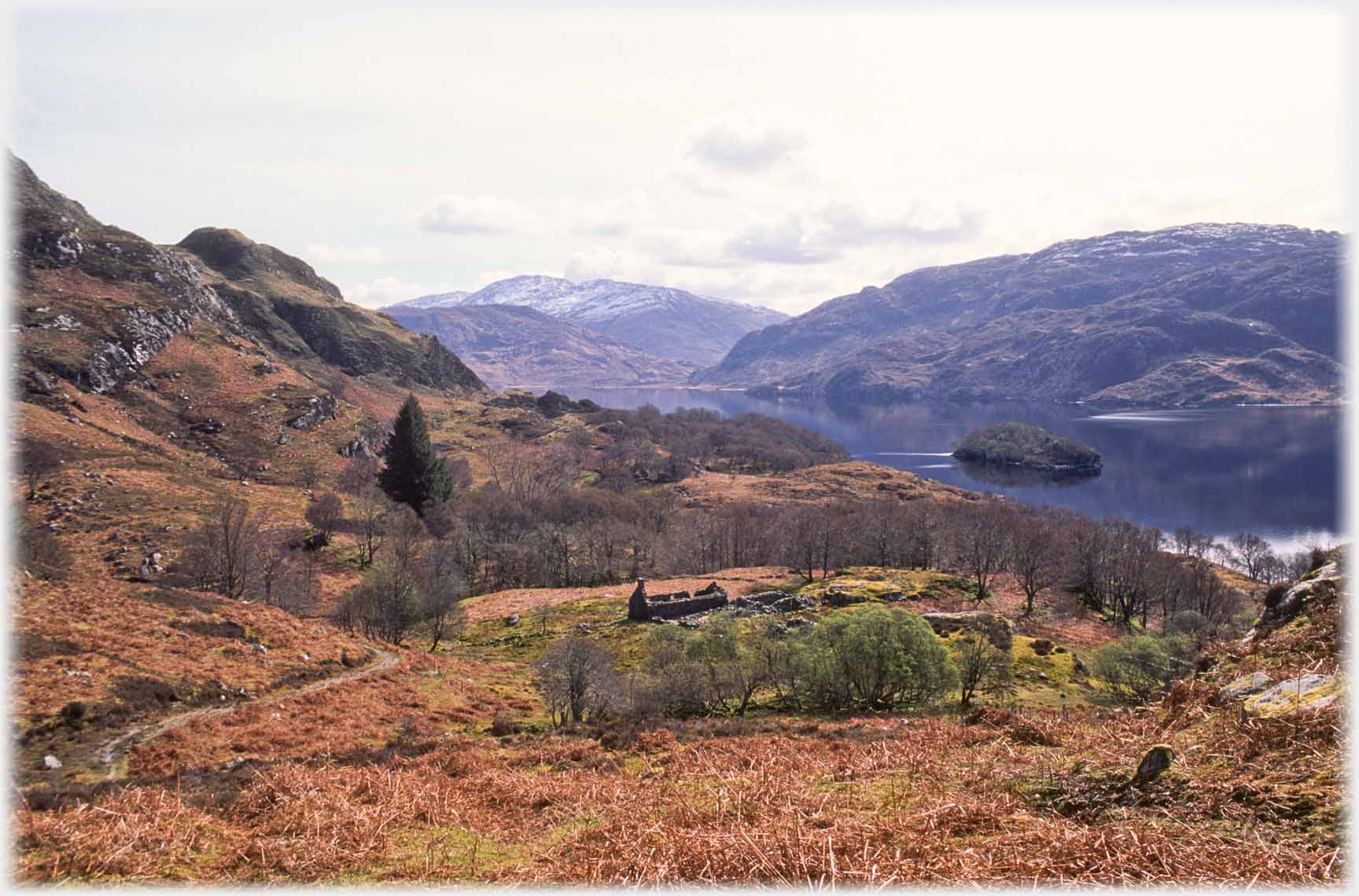 Brown ruined cottage in brown landscape, loch beyond.