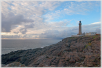 Lighthouse above rocks and sea.