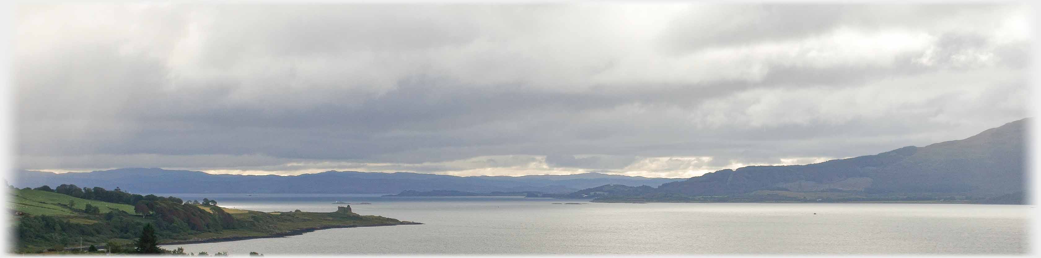 Heavy grey cloud over sea, promontary with building.