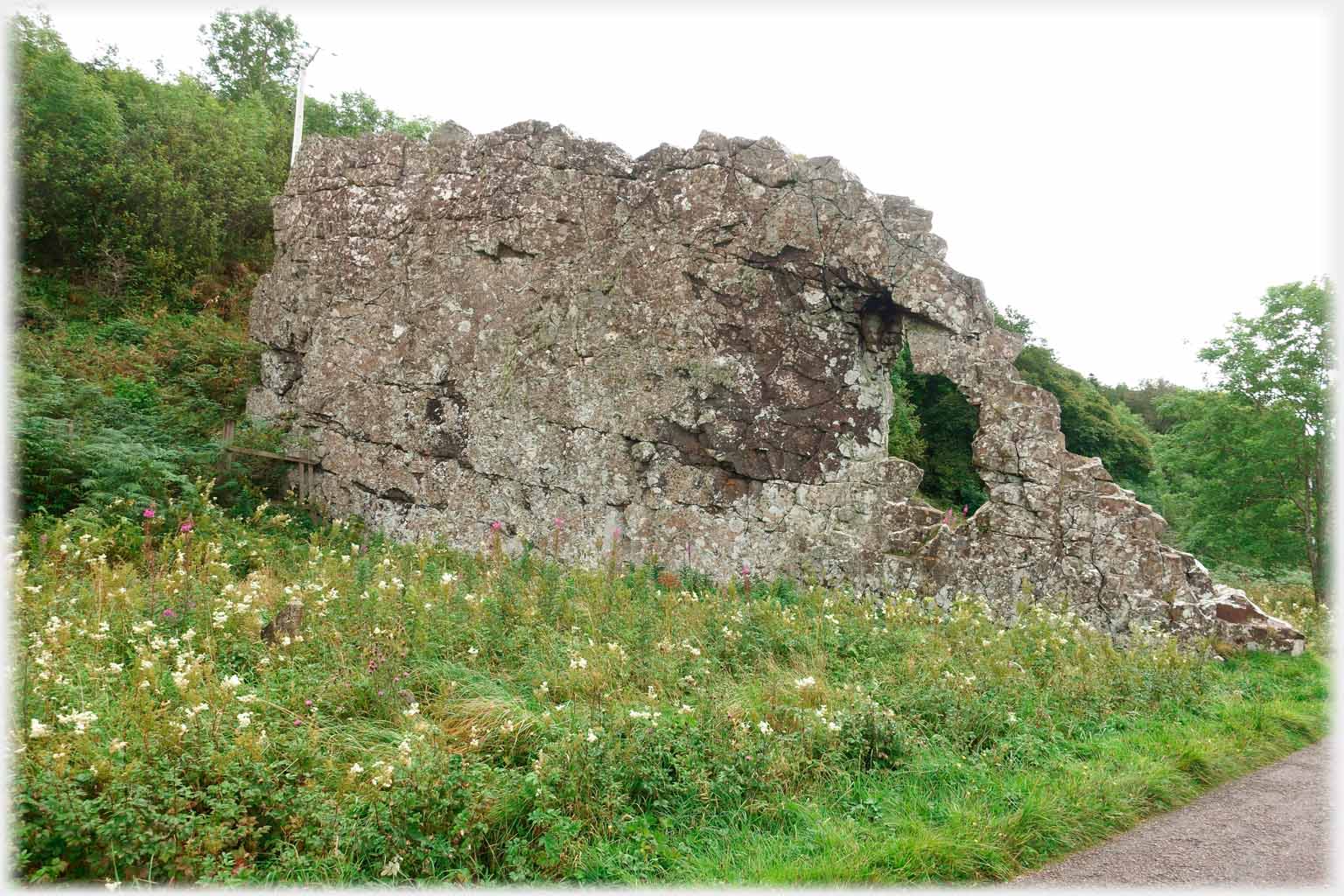 Stone wall shaped object in grass by road.