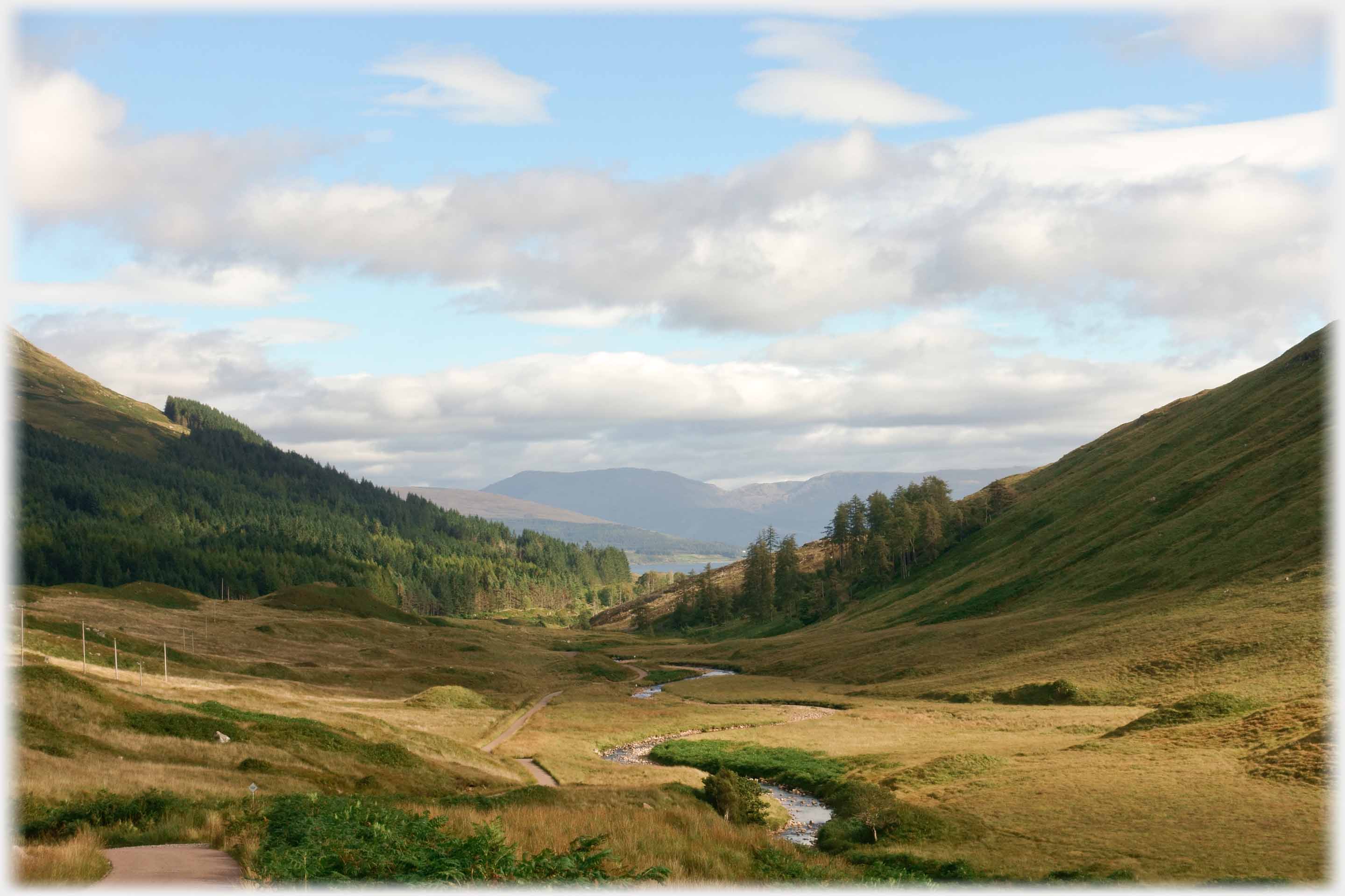 Wide valley with glimpse of sea and hills in the distance.