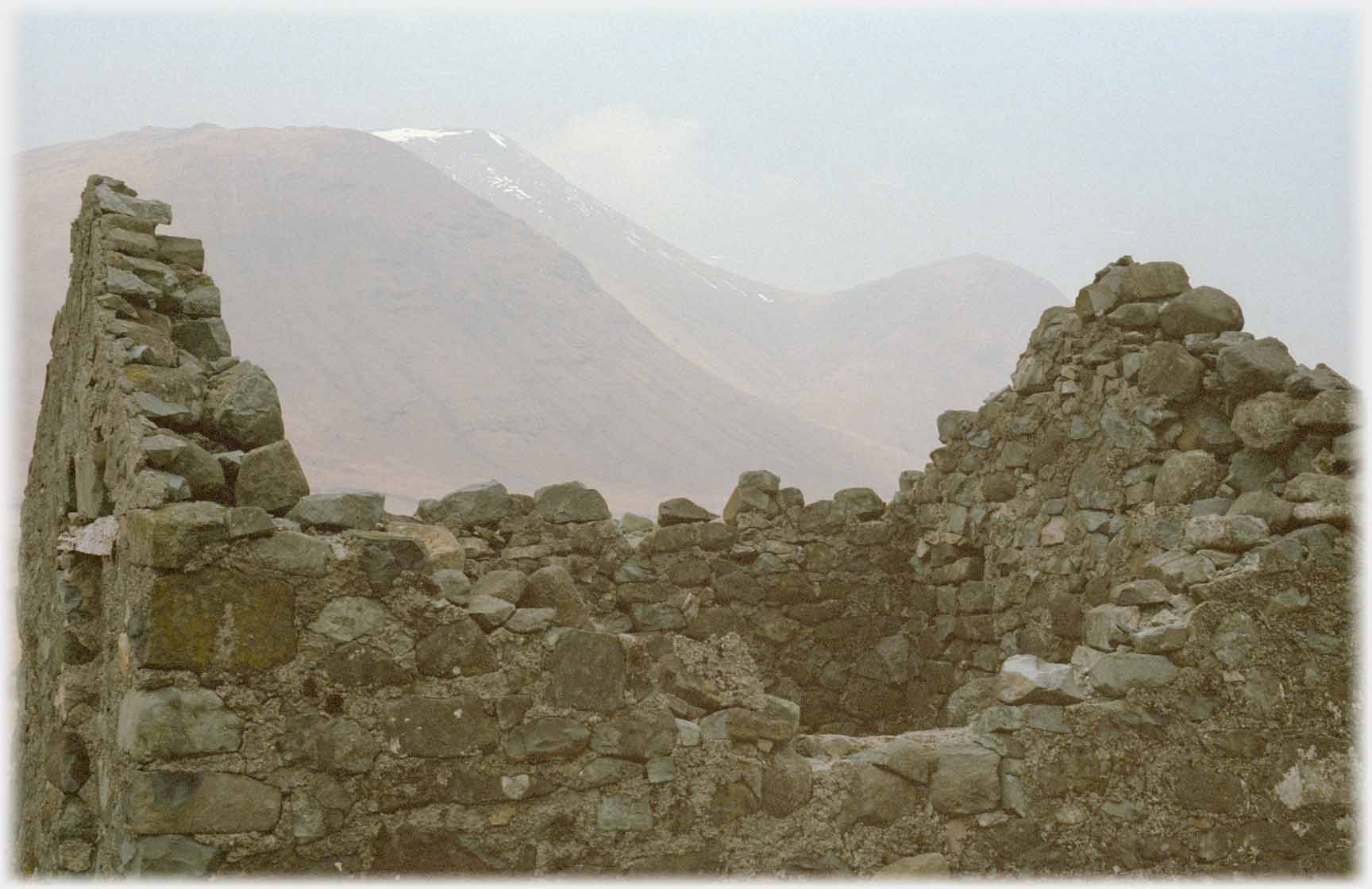 Close shot of small ruined house with hills beyond.