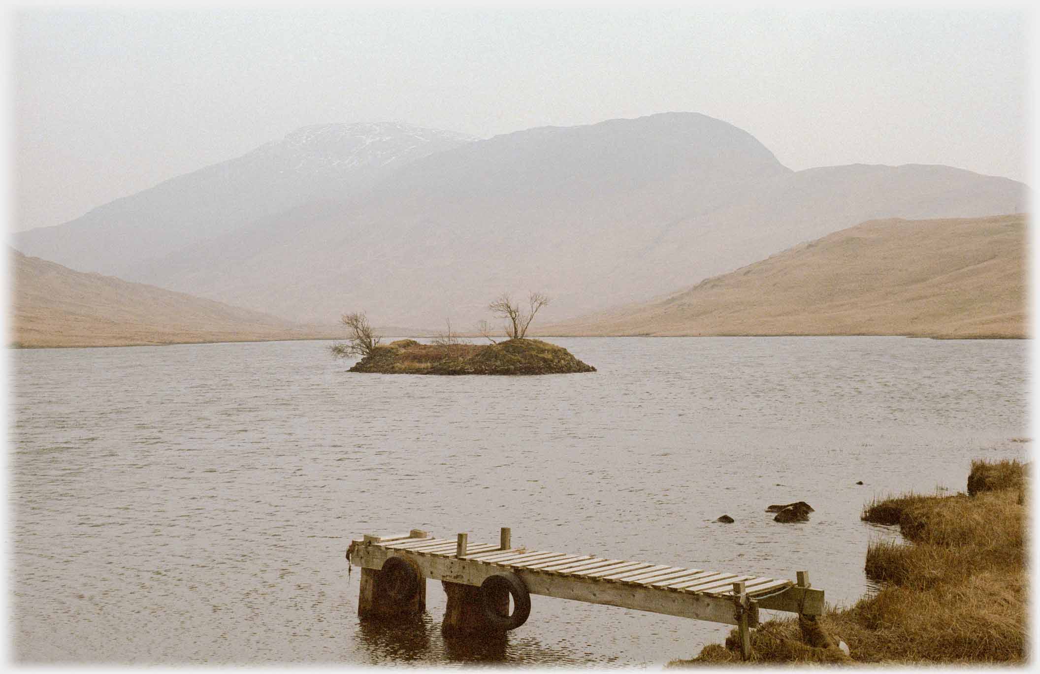Jetty by loch with small islet and hills beyond.