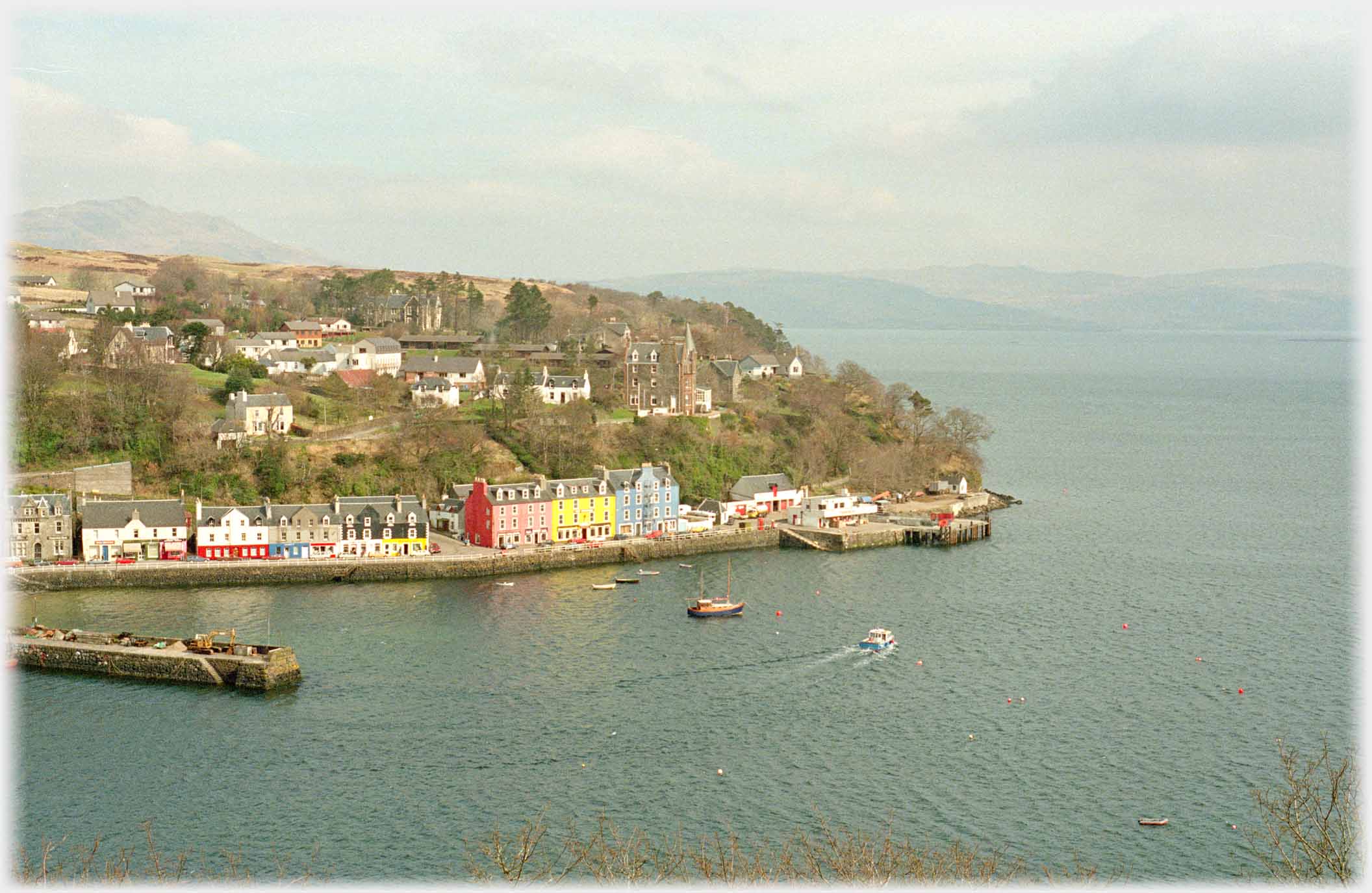 Brightly coloured houses near headland with hills across the sea.