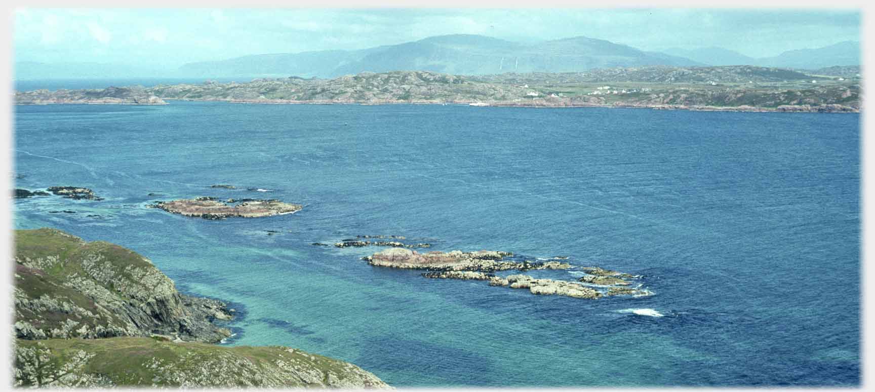 Turquoise sea with rocks and far hills.