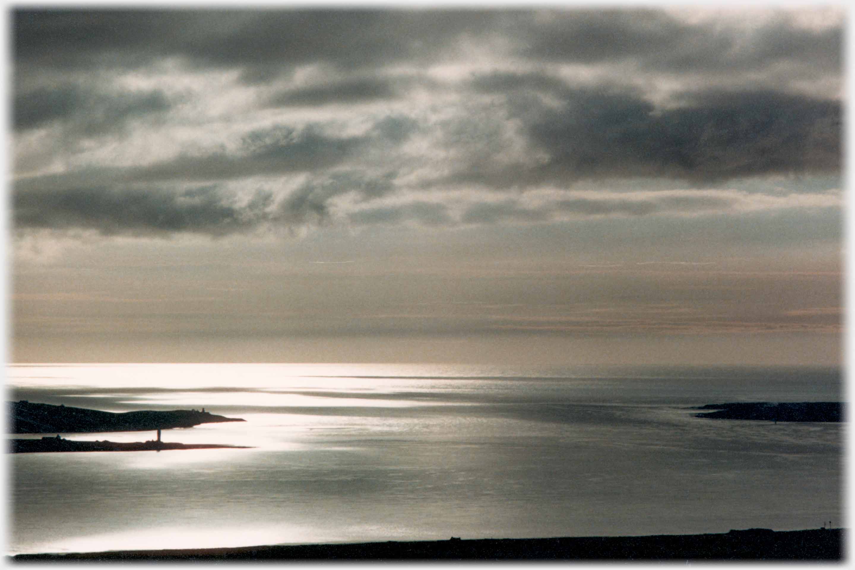 Evening light with low clouds reflected in the sea, land silhouetted.