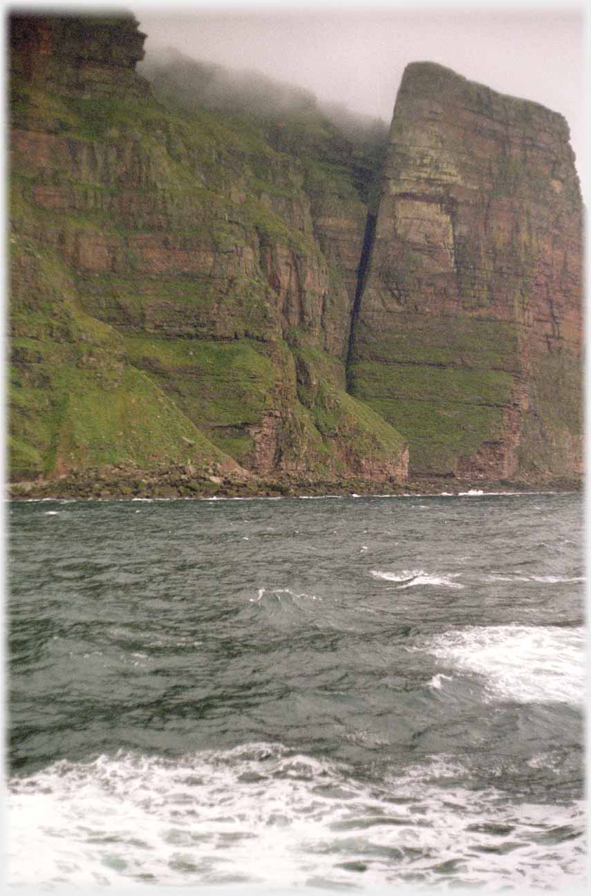 Bastion at an angle with top of cliffs in cloud.