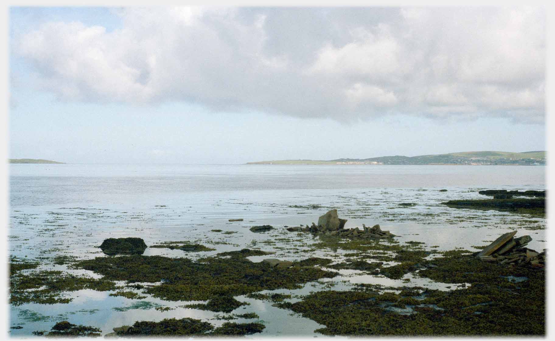 Foreground of the edge of the sea, low land in the distance.