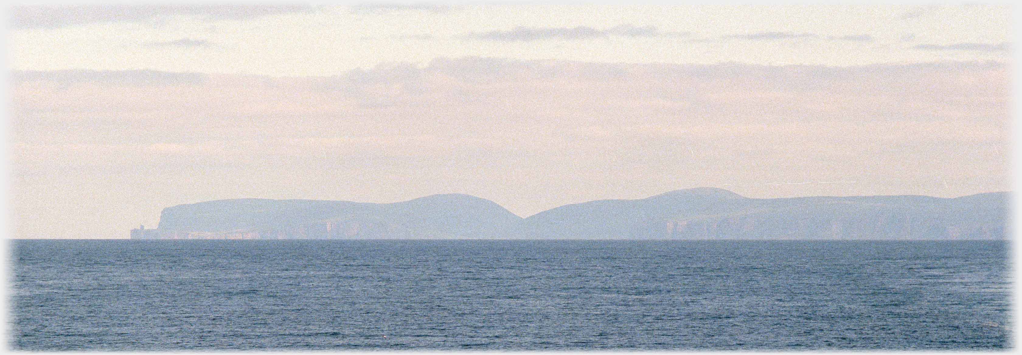 Silhouette of hills on island in evening across the sea.