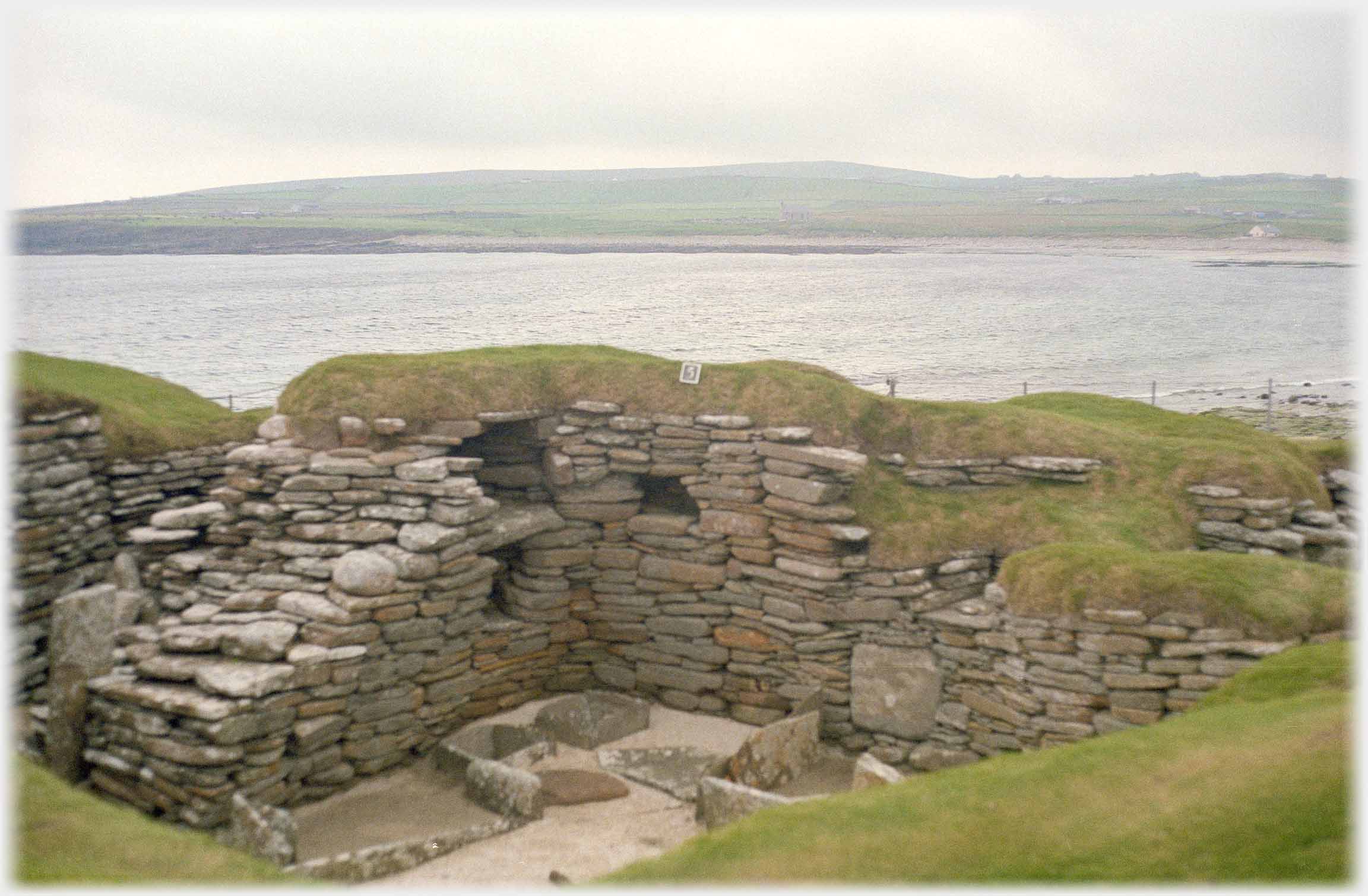 Turfed wall of slabs forming room with sea beyond.