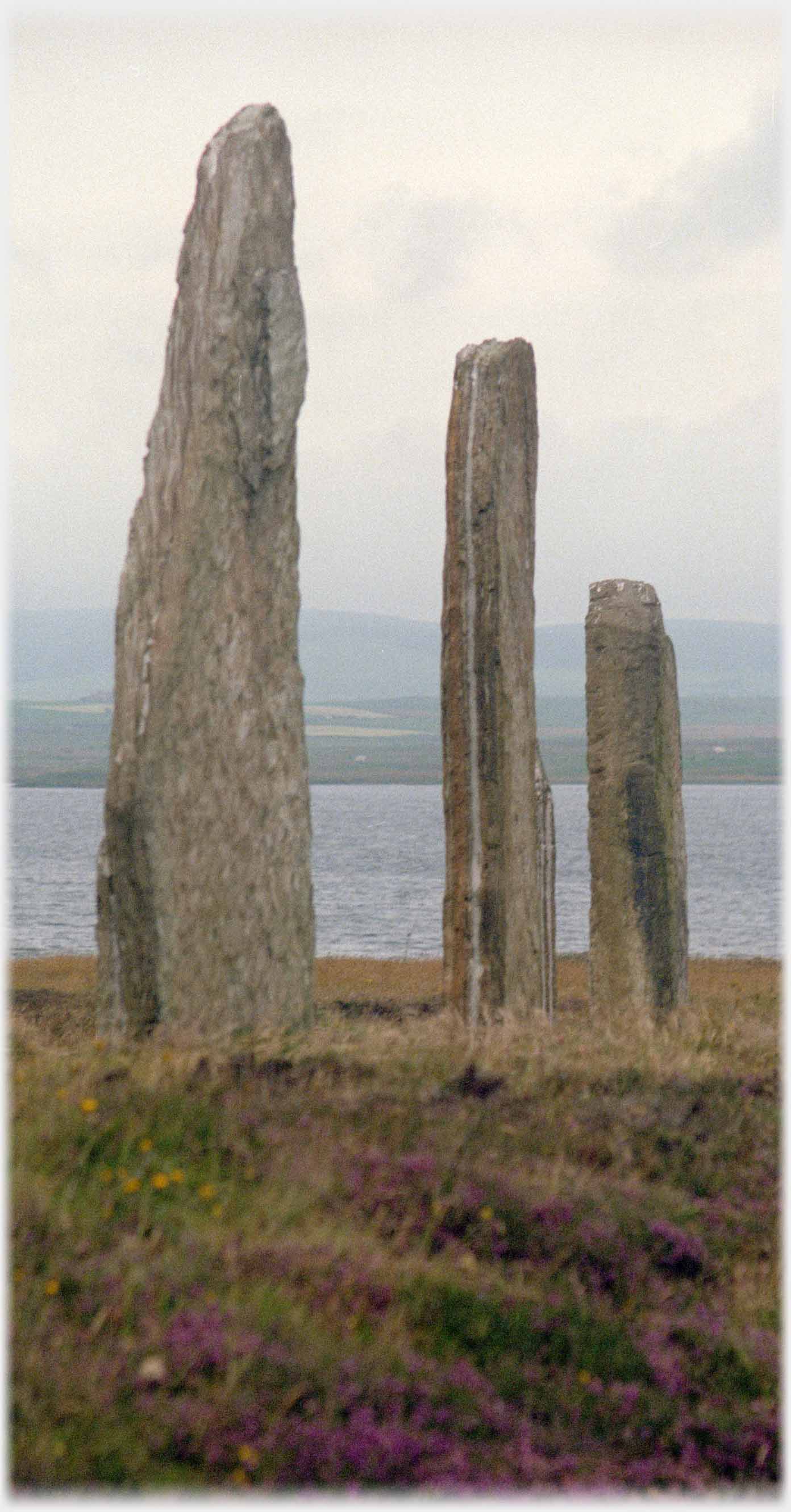 Three standing stones with sea beyond.
