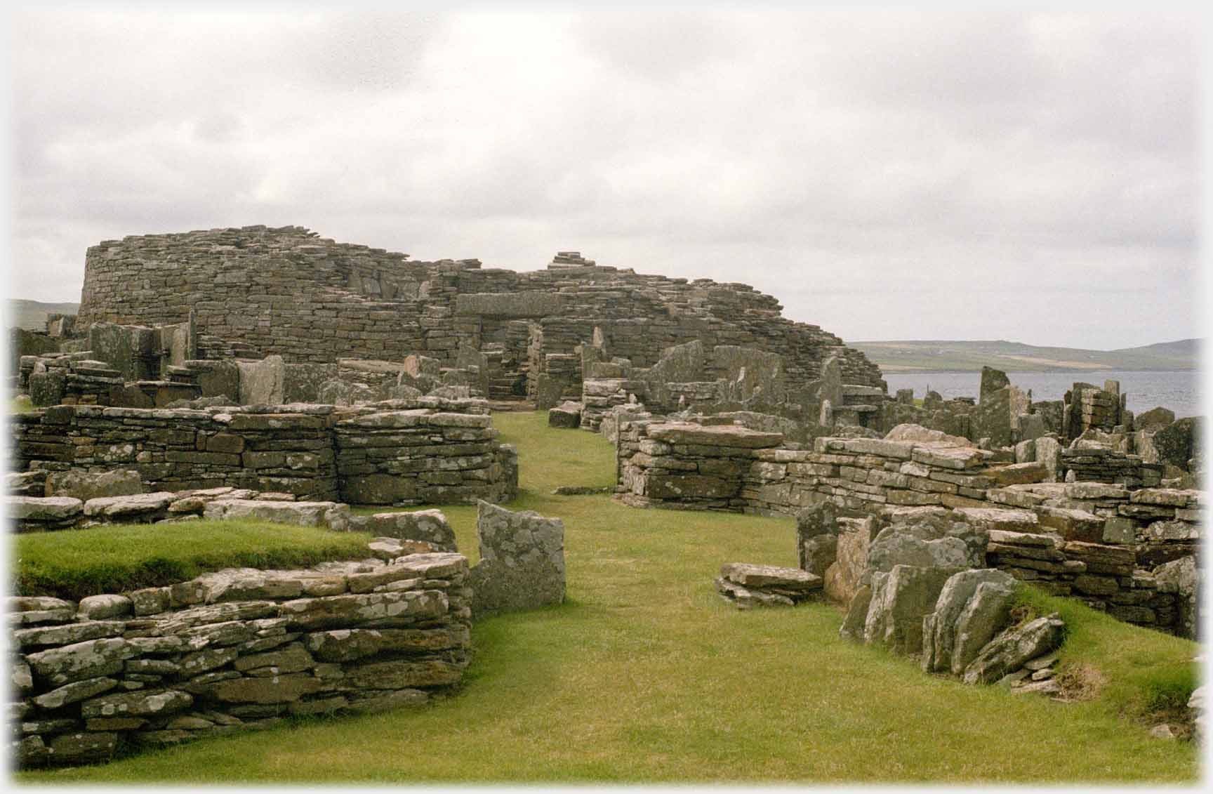 Looking along central path with ruined houses on both sides and ruin of broch ahead.