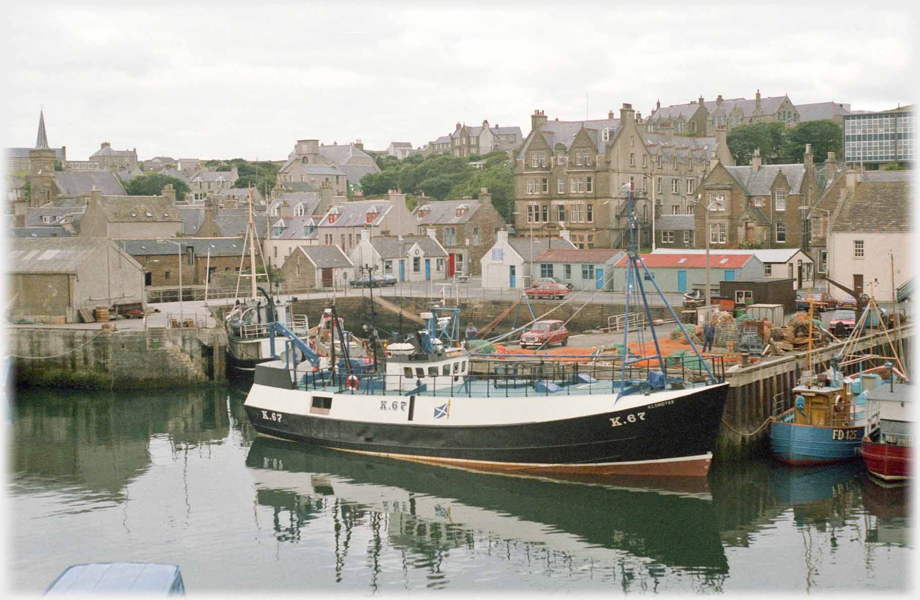 Houses around harbour, boat across harbour mouth.