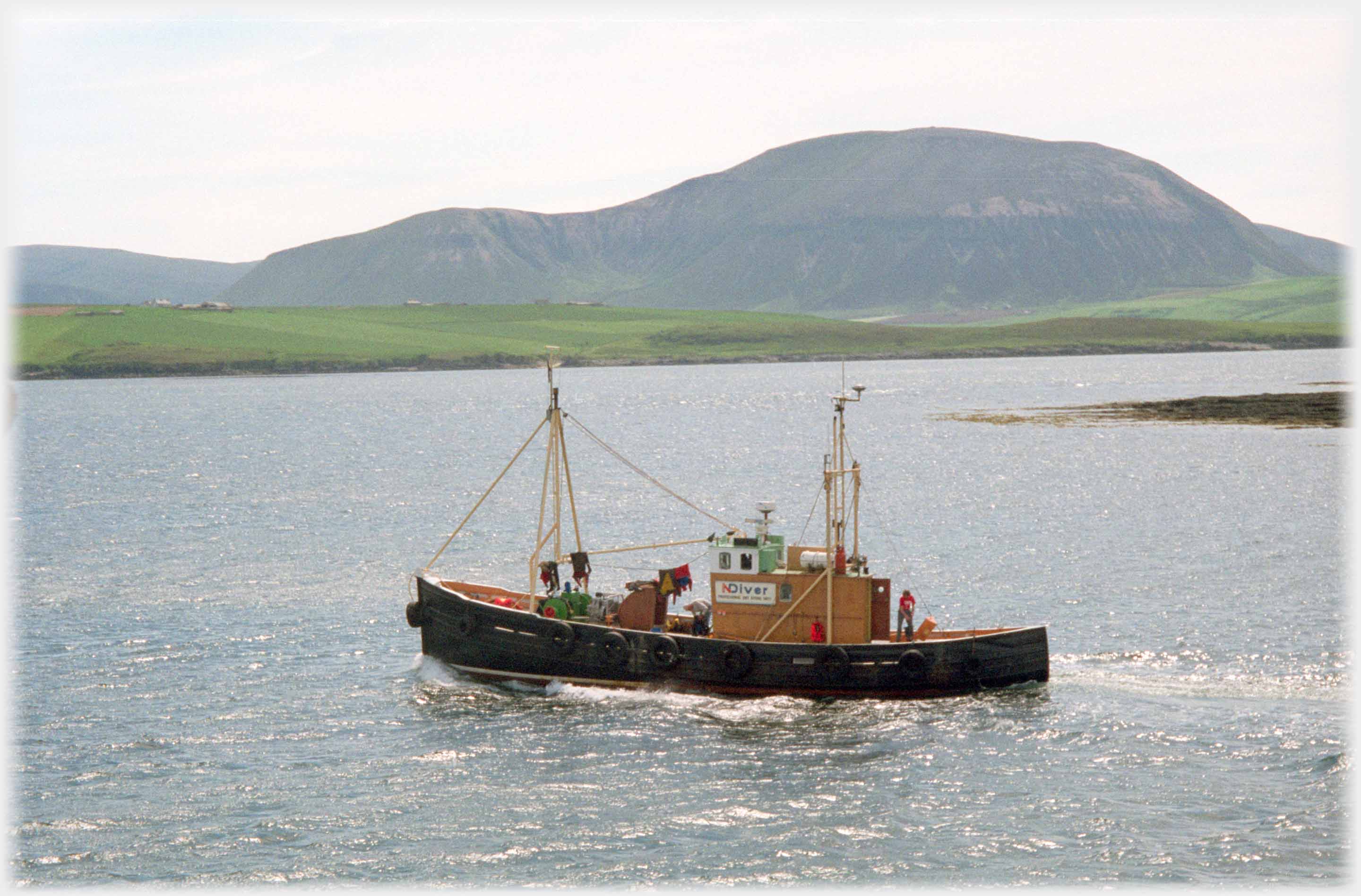 Small fishing boat moving in sea with Hoy hill behind.
