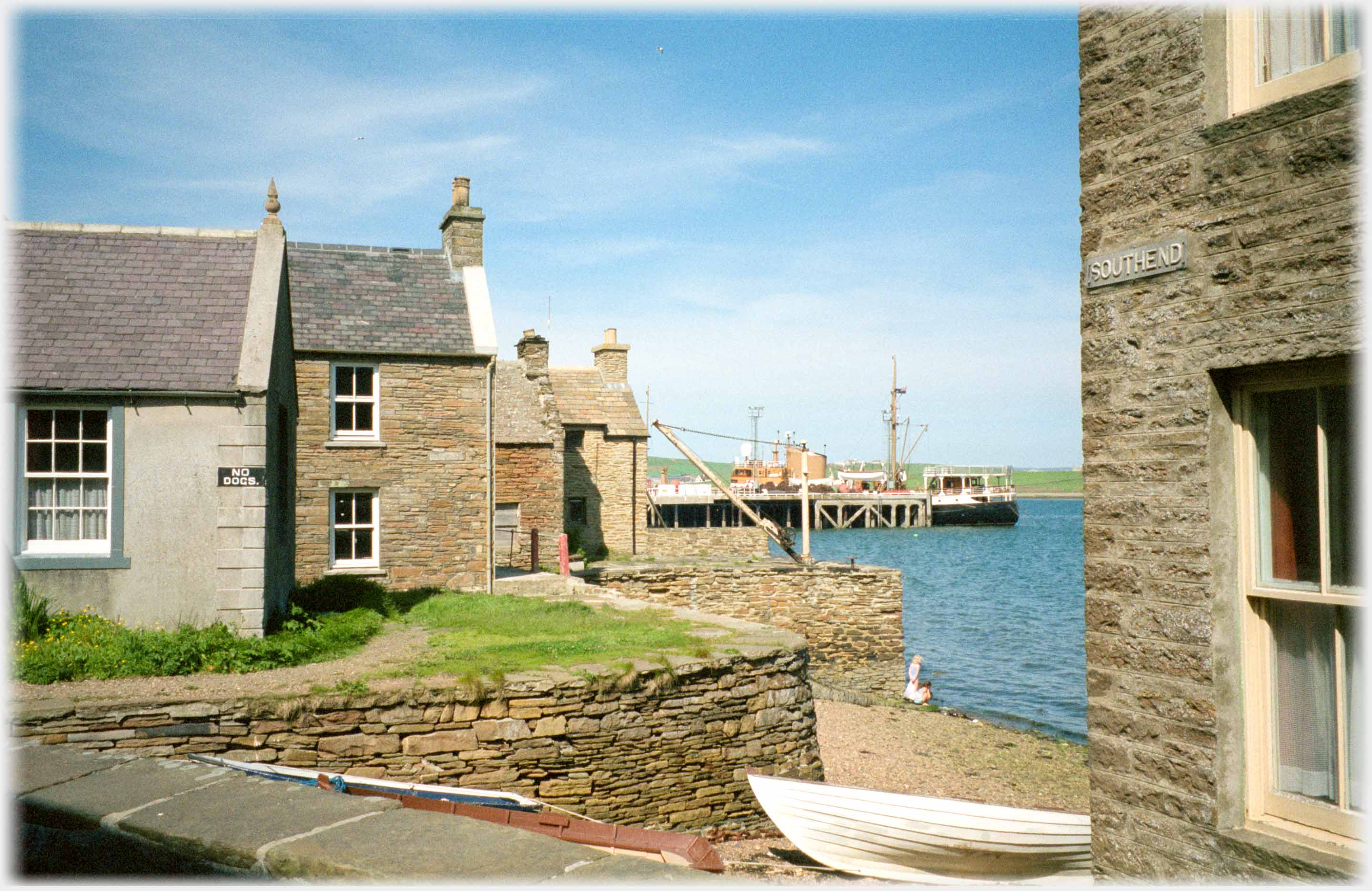 Looking between houses at the sea and pier with boat.