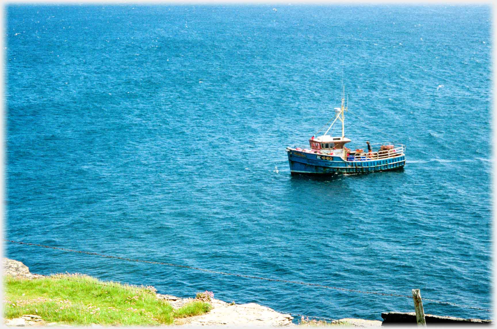 Small fishing boat in sea just off cliffs.