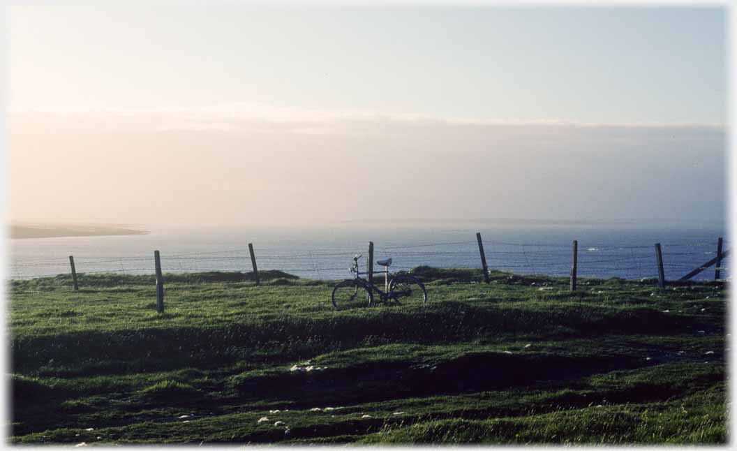 Wire fence with bike leaning on it and sea beyond.