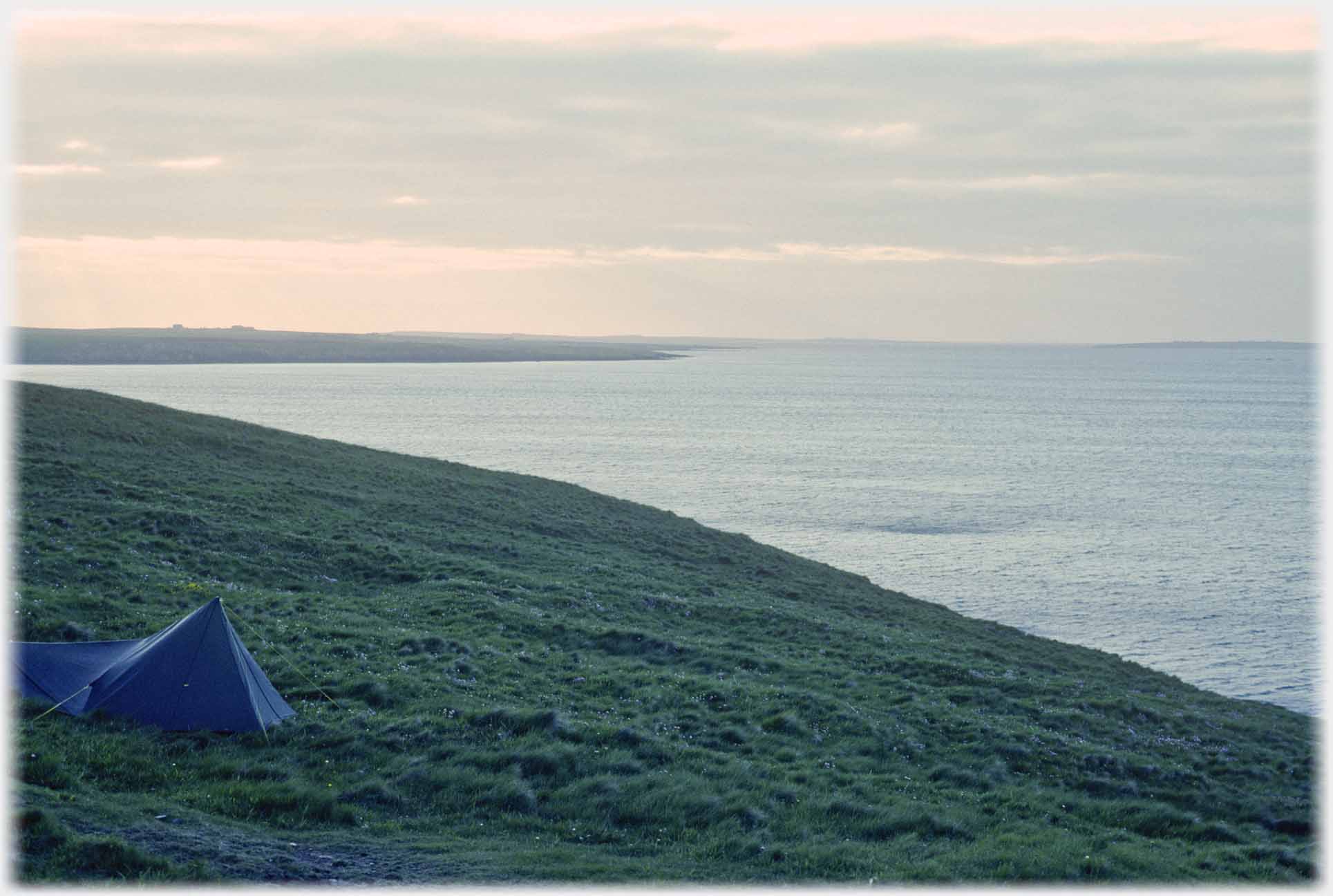 Tent pitched on grassy hillsde overlooking sea.