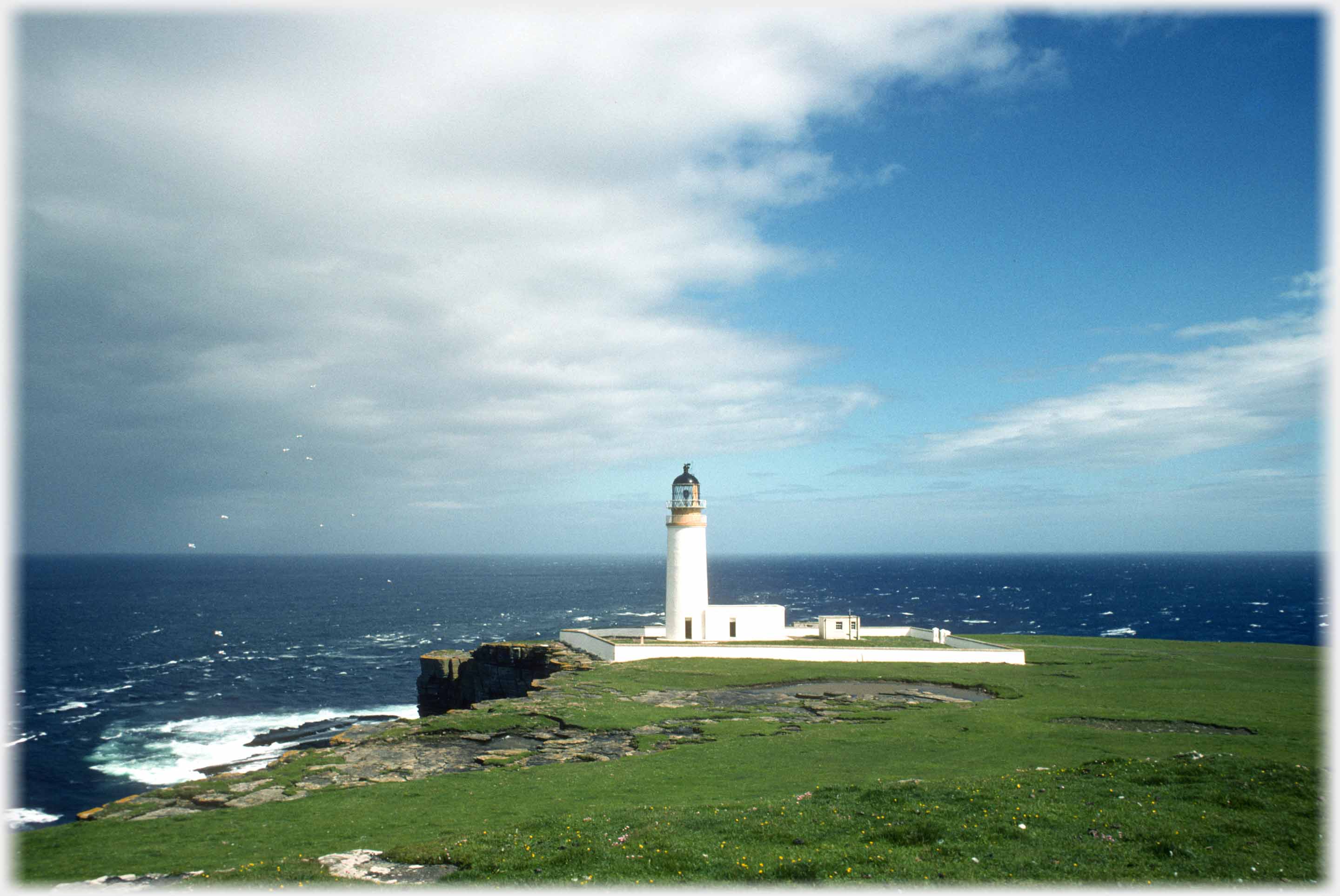 Lighthouse on headland with sea beyond.