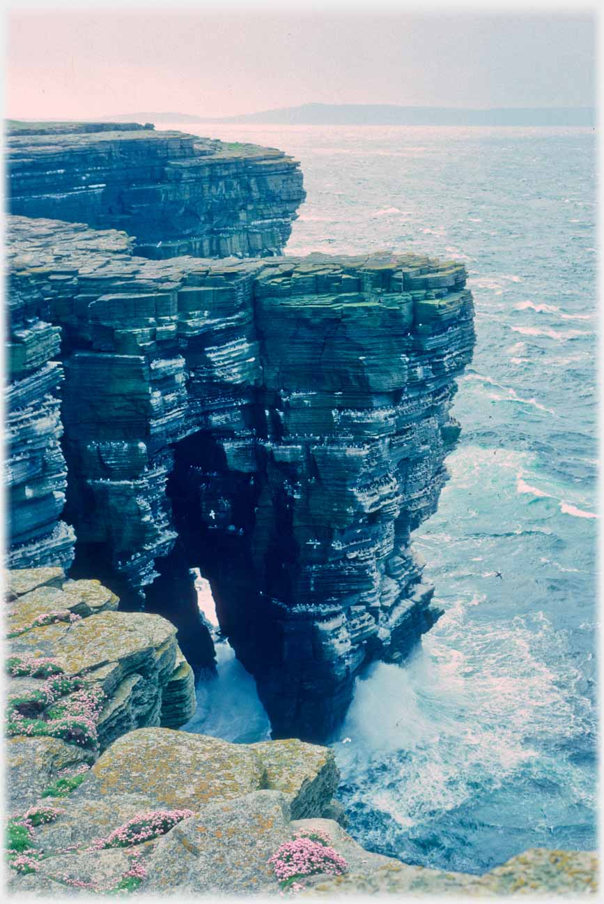 Cliffs with caves hollowed out below and water passing right through.