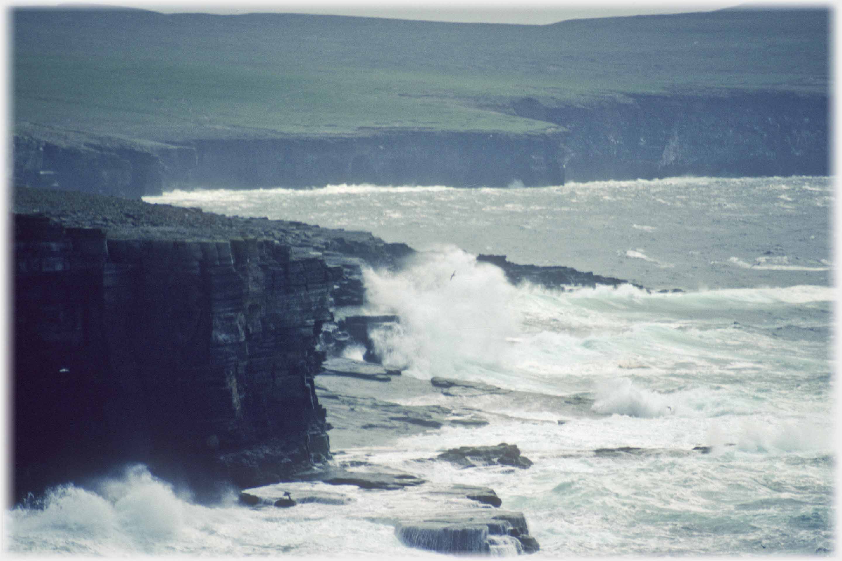 High breakers over rocks below cliffs.