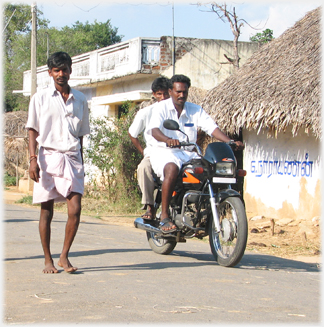 Man walking and men on motorbike.